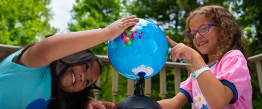 Two young girl scouts smiling with colorful globe