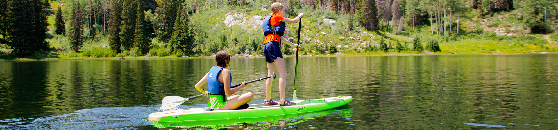  two girls paddleboarding across a lake 