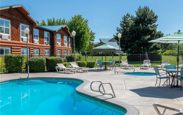 a blue in-ground pool pictured on a sunny day with a hotel in the background
